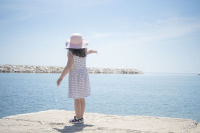 Rear view of young woman standing on sea shore against sky