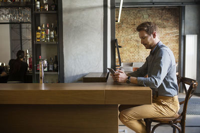 Side view of businessman using tablet computer while sitting at bar counter in hotel