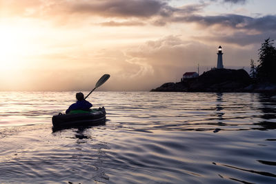 Man on boat in sea against sky during sunset