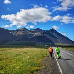 Rear view of friends walking on road leading towards mountain against sky