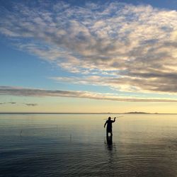 Silhouette man fishing in sea against cloudy sky