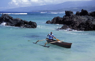 Man rowing outrigger on sea against rock formation