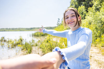 Portrait of young woman with arms raised against sky