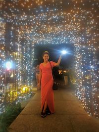 Full length portrait of woman standing against illuminated lights at night