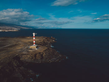 Lighthouse by sea against sky