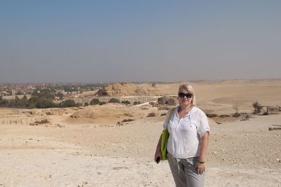 A plump young woman in light cotton clothes stands in the middle of a desert