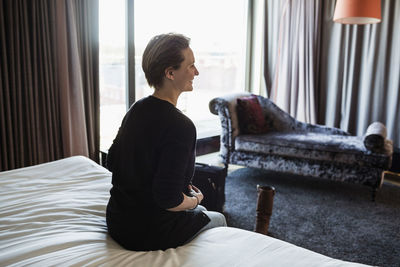 Rear view of smiling businesswoman sitting on bed in hotel room