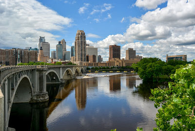 Arch bridge over river by buildings against sky