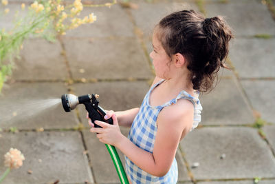 Young girl is watering plants in the backyard while wearing a bathing suit