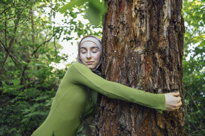 Portrait of young woman standing against tree trunk