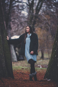 Young woman standing by tree trunk in forest