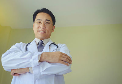 Portrait of confident doctor standing against wall at clinic
