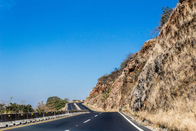 Road by mountain against clear blue sky