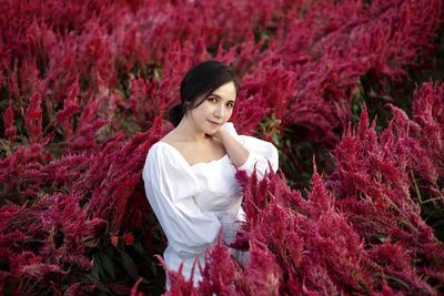 Portrait of smiling young woman standing against red plants