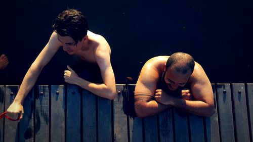 High angle view of shirtless male friends standing at jetty in lake