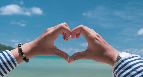 Midsection of man making heart shape against sky