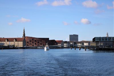 View of buildings by river against cloudy sky