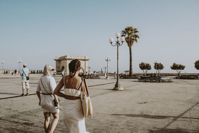 Friends walking on street against clear sky