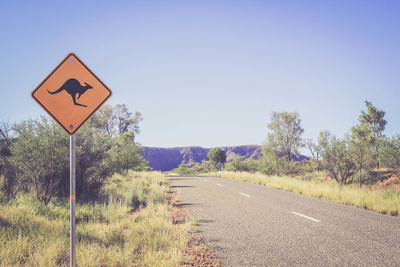 Kangaroo crossing sign by road against sky