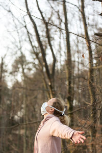 Woman wearing mask standing with arms outstretched in forest