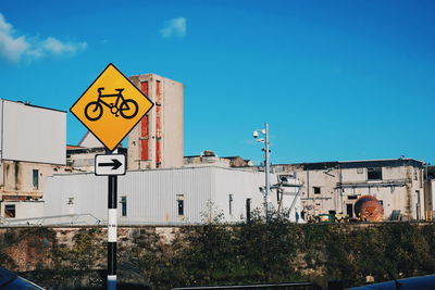 Road sign by building against blue sky