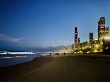 View of illuminated buildings at beach against blue sky