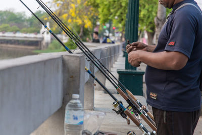 Midsection of man holding fishing rod by retaining wall 