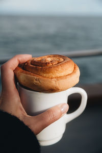 Close-up of hand holding coffee and cinnamon bun