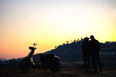 Rear view of silhouette couple standing by motorcycle against sky during sunset