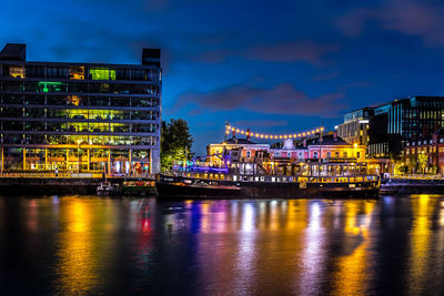 Illuminated buildings by river against sky at night