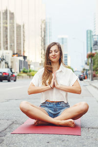 Smiling woman mediating while sitting on road in city
