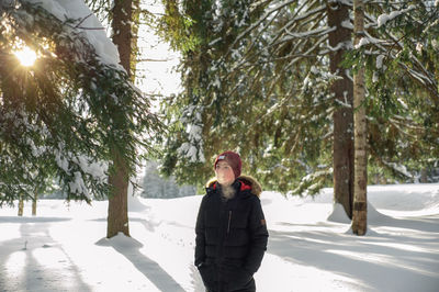 A teenage boy walks through a snow-lowned forest on a frosty winter sunny day. steam from the mouth