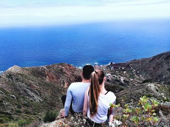 Rear view of people sitting on rock looking at sea