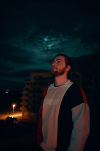 Young man looking at illuminated city against sky at night