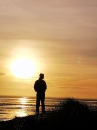 Silhouette man standing on shore against sky during sunset