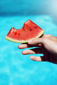 Cropped hand holding melon slice against swimming pool