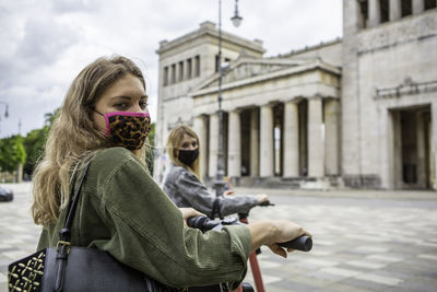 Female friends wearing masks with electric push scooters standing on street