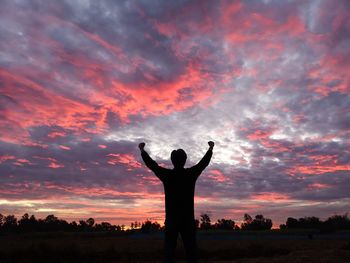 Silhouette man with arms raised standing against sky during sunset