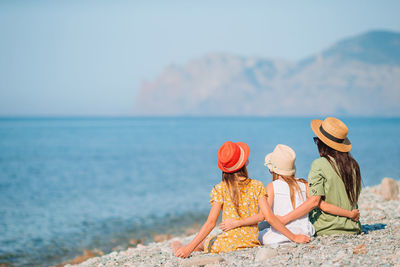 Rear view of women sitting at beach against sky