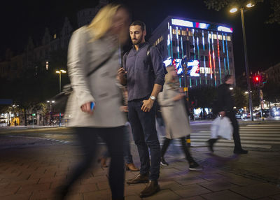 Full length of man using mobile phone on sidewalk in city at night