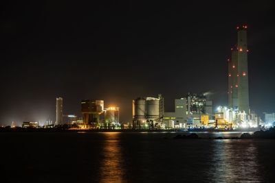 Illuminated buildings by river against sky at night