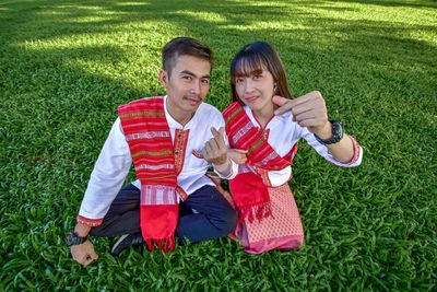 Portrait of smiling couple sitting on field against sky