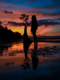 Silhouette woman standing on beach against sky during sunset