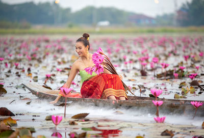 Young woman holding water lilies sitting in boat on lake
