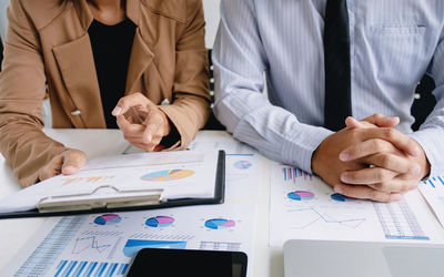 Midsection of coworkers discussing graphs on desk in office