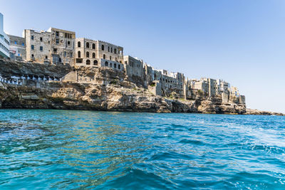 Sea by rocks against clear blue sky