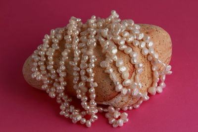 Strings of white freshwater pearls displayed on a rock against a bright pink background.