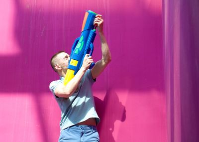 Man aiming with squirt gun against pink wall