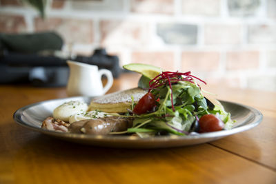 Close-up of pancakes with salad and sausage served in plate on wooden table