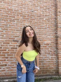 Portrait of smiling young woman against brick wall